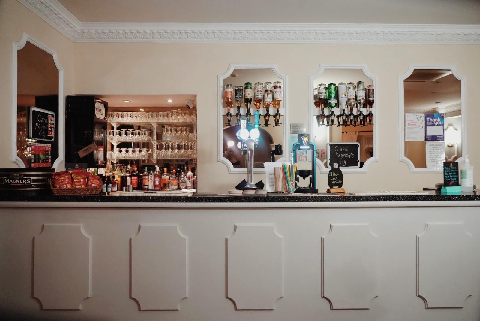 A bar area with multiple liquor bottles, a cash register, and a sign indicating card payments are accepted.