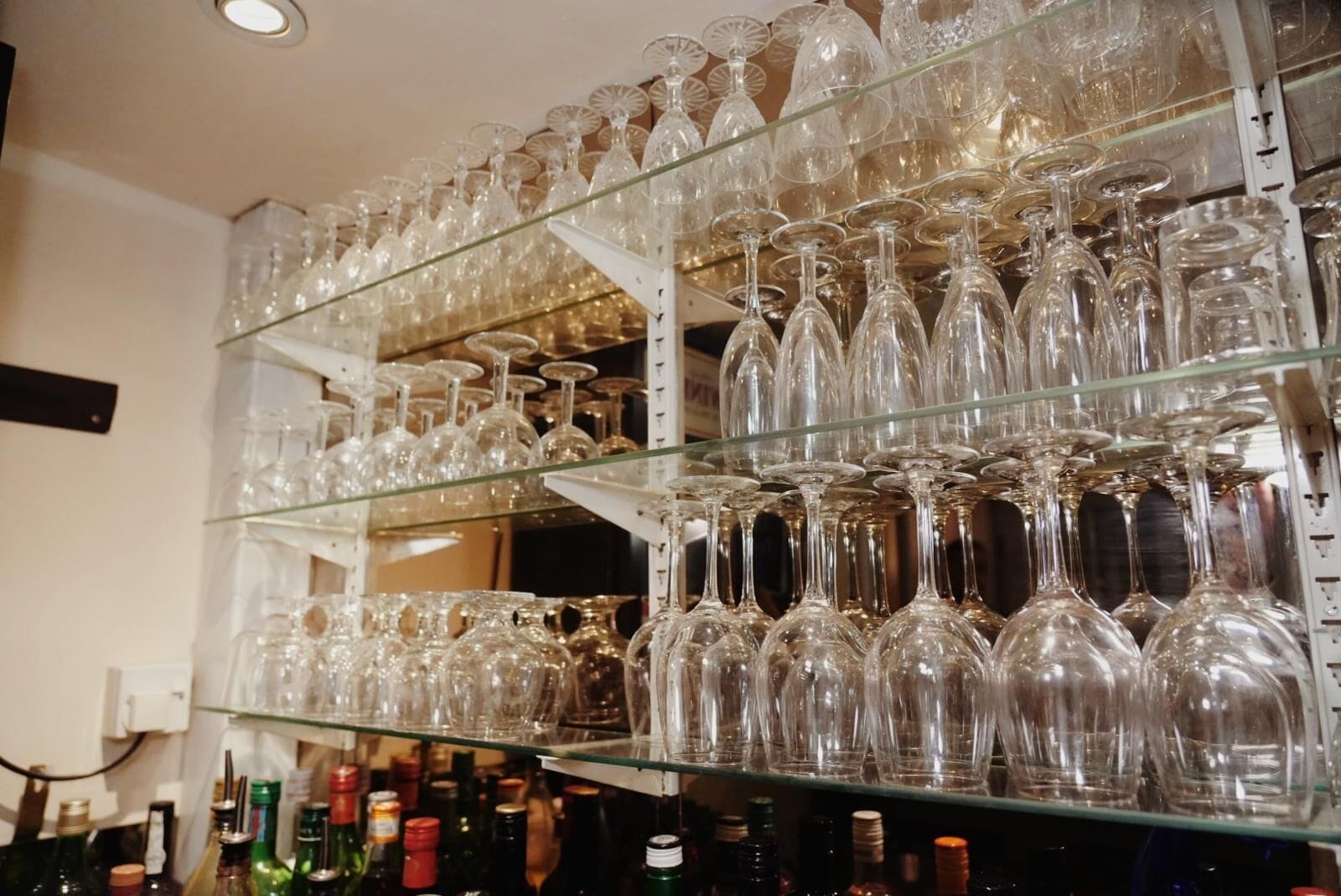 A storage area with multiple shelves filled with clear glass bottles and wine glasses.