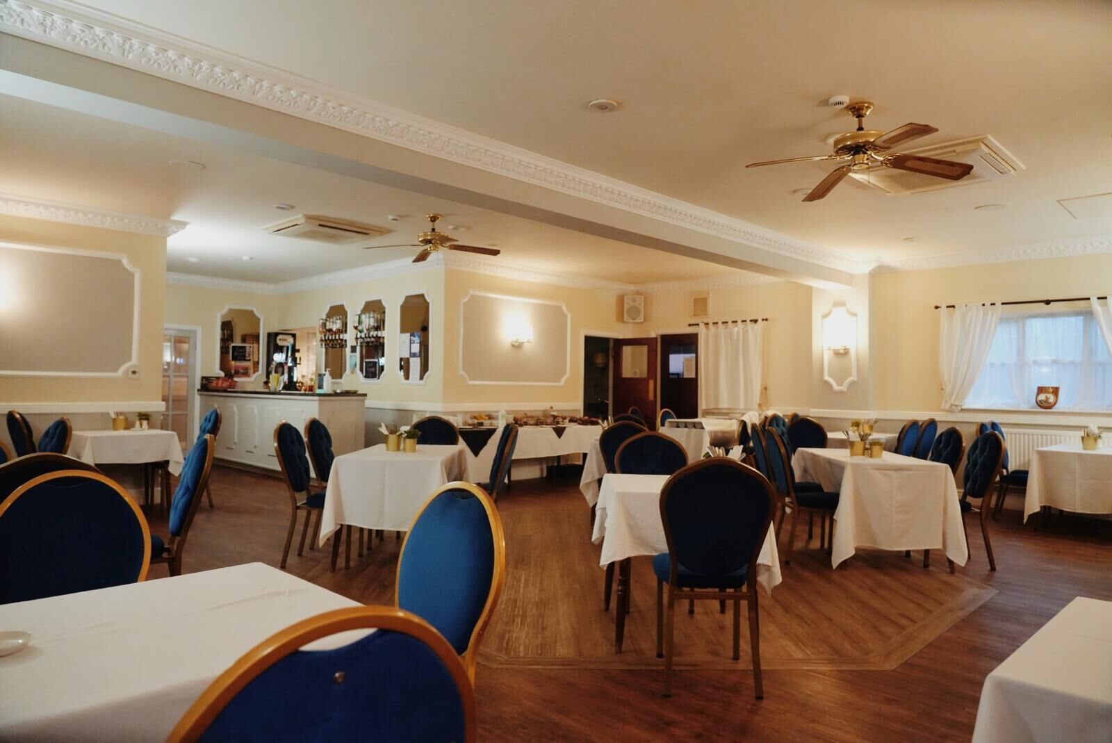 A dining area with round tables and blue chairs, a bar area, and ceiling fans.