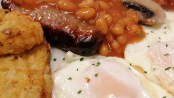 A plate of breakfast food including beans, bacon, mushrooms, hash browns, and fried eggs.