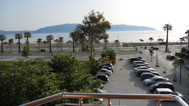Un estacionamiento con coches y vistas a la playa y montañas al fondo.
