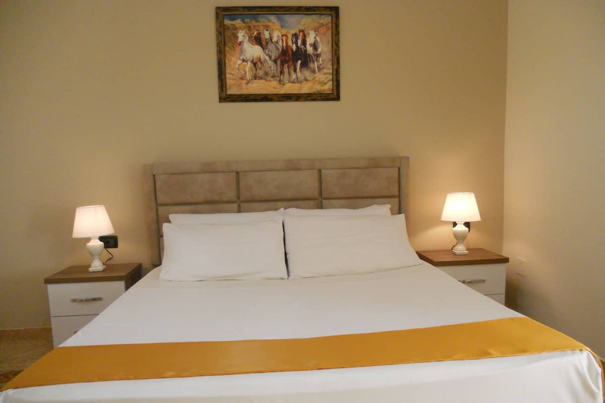 Une chambre d’hôtel avec un grand lit, deux tables de chevet avec des lampes, une tête de lit et un tableau au mur.