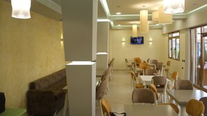 Un comedor moderno con mesas y sillas altas, un televisor de pantalla plana montado en la pared e iluminación colgante.