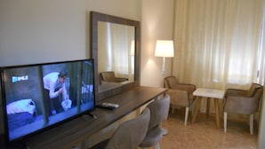 Habitación de hotel con televisión, escritorio, dos sillas, lámpara y ventana con cortinas.