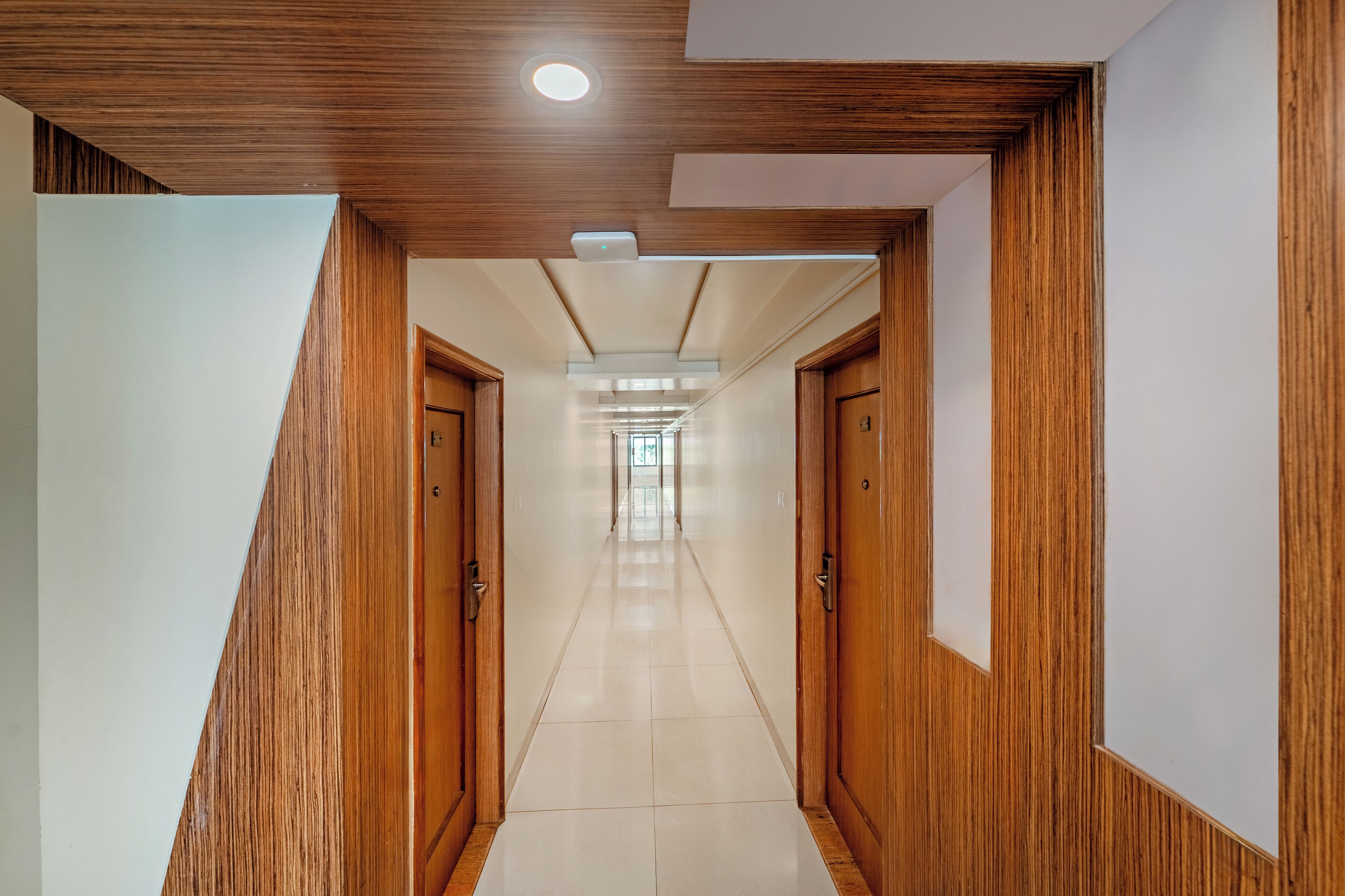 A long, narrow hallway with wooden paneling on the walls and ceiling, leading to a bright room at the end.