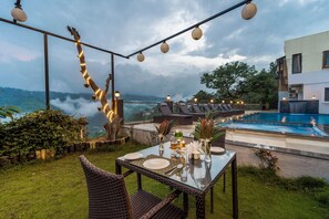 Un área de comedor al aire libre con una mesa de vidrio, sillas de mimbre y una piscina al fondo.