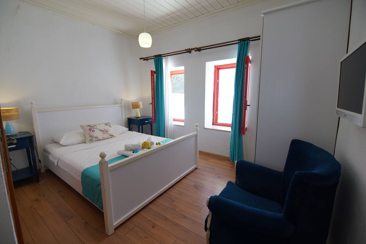 A bedroom with a bed, bedside tables, a chair, a TV, and curtains.