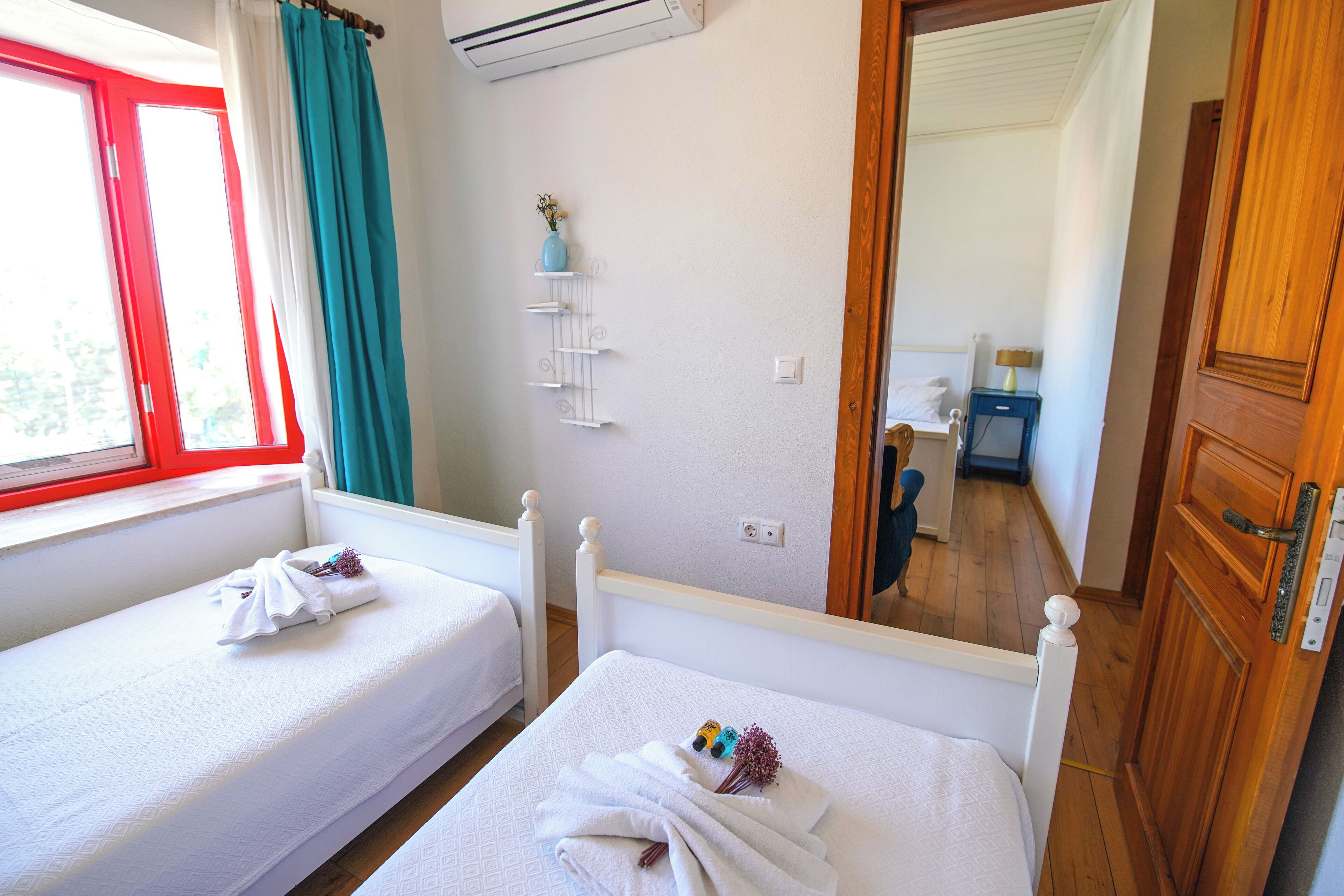 A hotel room with two single beds, a window with curtains, a wall-mounted air conditioner, a mirror, and a wooden door.