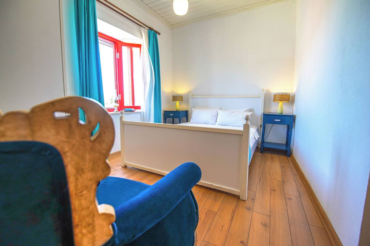 A bedroom with a bed, two bedside tables, a chair, and a window with curtains.
