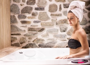 A woman in a bathtub with a stone wall background. - Hotel Riva Sport & Wellness (Vione)