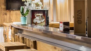 A wooden interior with a bar area, wooden stools, a television, and a refrigerator. - Hotel Riva Sport & Wellness (Vione)