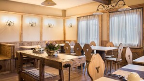 A wooden dining area with tables and chairs, a chandelier, and wall-mounted lights. - Hotel Riva Sport & Wellness (Vione)