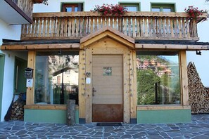A wooden building with a balcony, a wooden door, and a stone-paved entrance. - Hotel Riva Sport & Wellness (Vione)