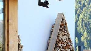 A stack of firewood against a building's exterior wall, with a wooden structure above it. - Hotel Riva Sport & Wellness (Vione)