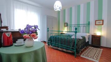 Una habitación con cama, una mesa con un jarrón de flores, una tetera y una lámpara.