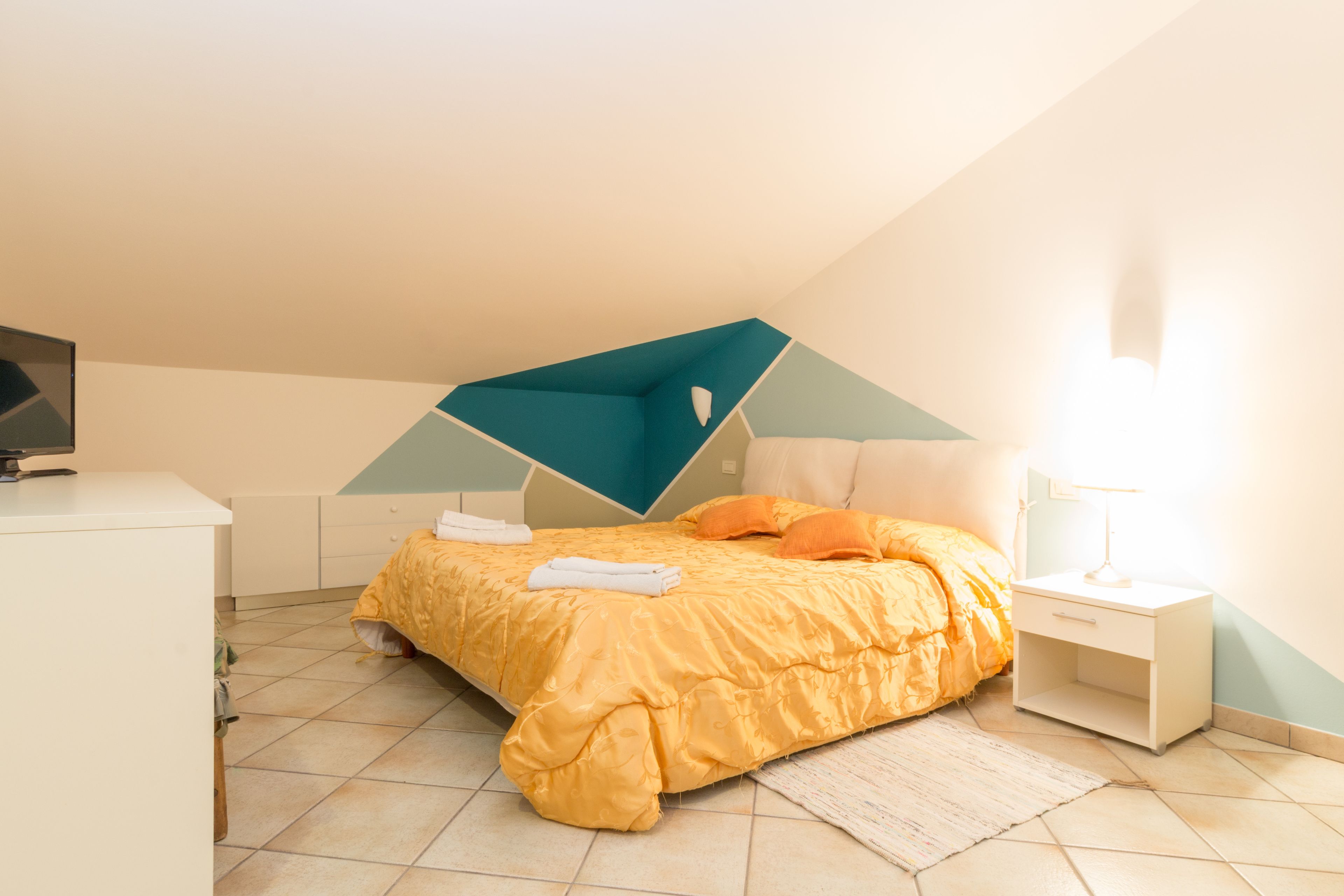 A bedroom with a bed, a nightstand, a lamp, and a TV.