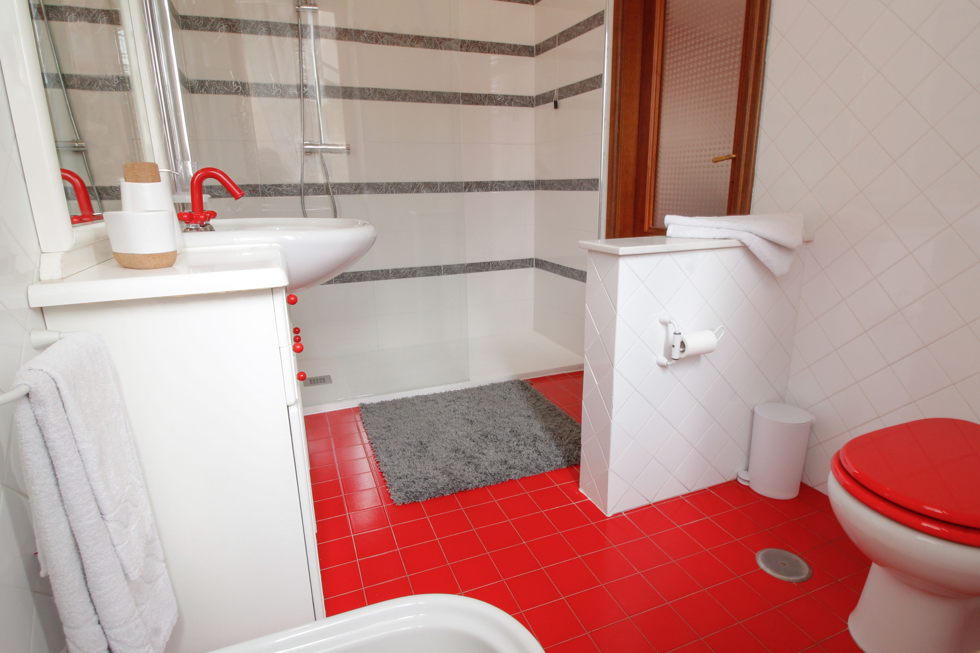 A bathroom with a red-tiled floor, a white sink, a red toilet, and a shower area.