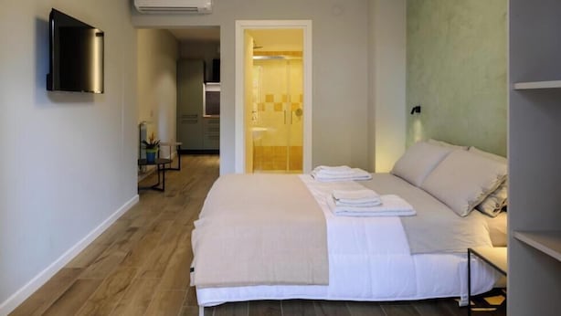Un dormitorio moderno con una cama grande, una mesita de noche, un televisor de pantalla plana montado en la pared y un equipo de aire acondicionado.