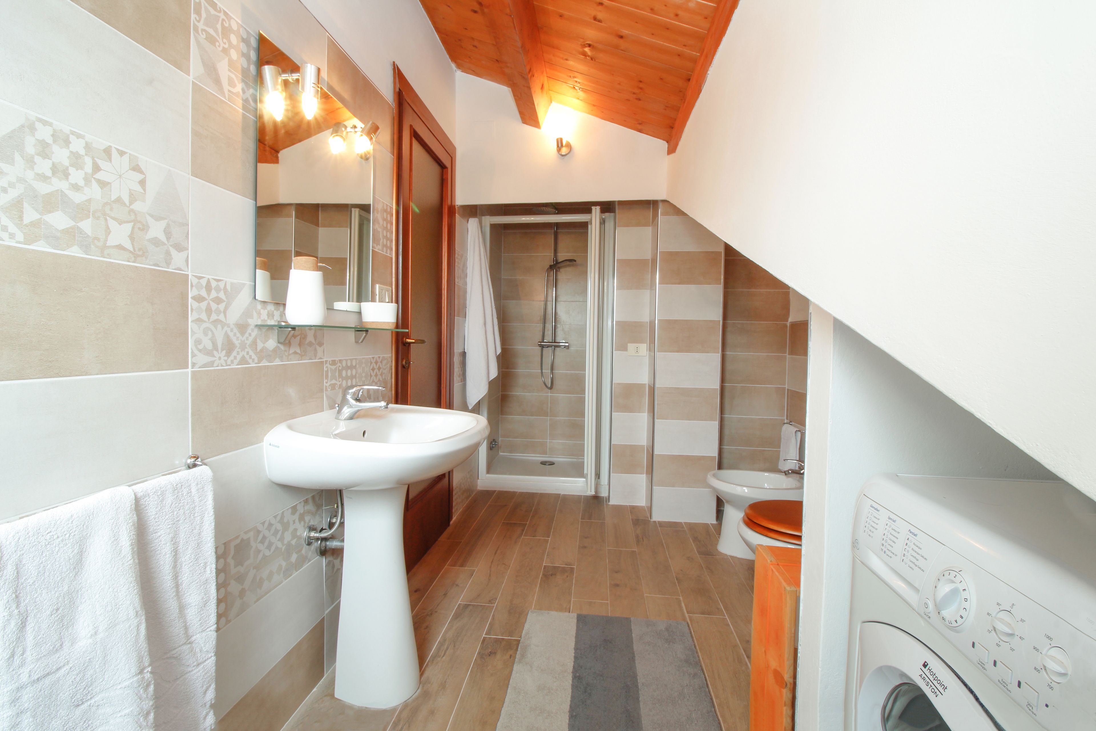 A bathroom with a sink, mirror, shower, toilet, and washing machine.