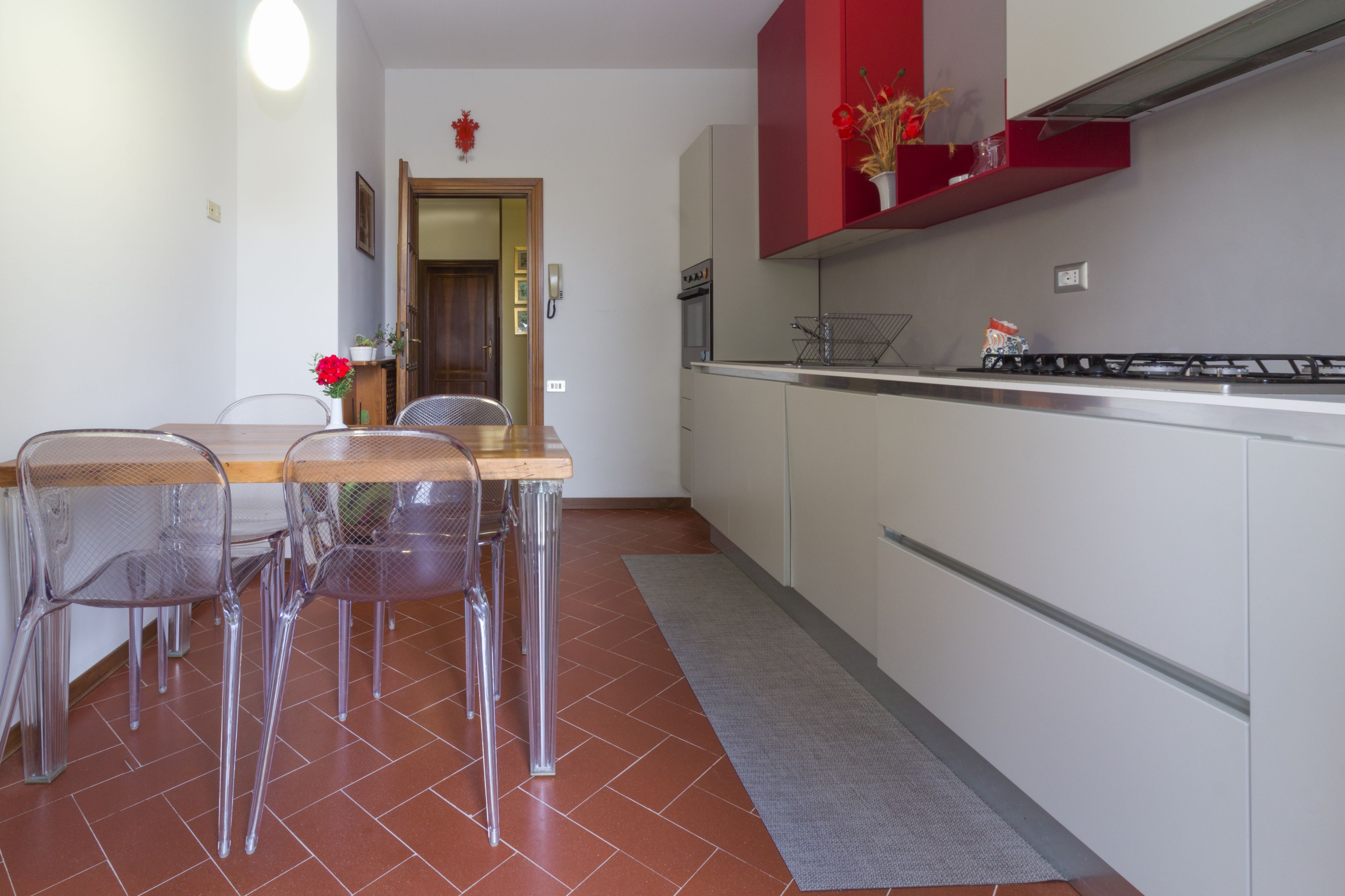 Una cocina con una mesa y sillas de madera, un armario rojo y un piso con baldosas.