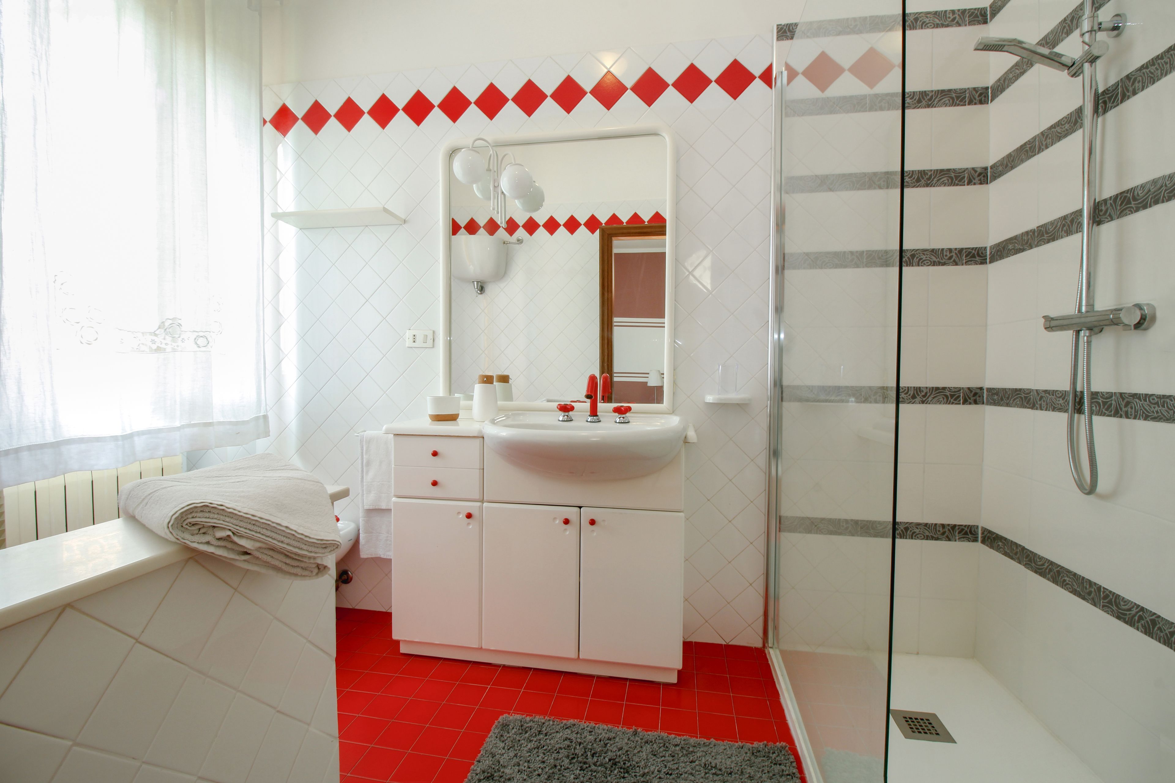 Un baño con un lavamanos blanco, espejo y suelo de baldosas rojas.