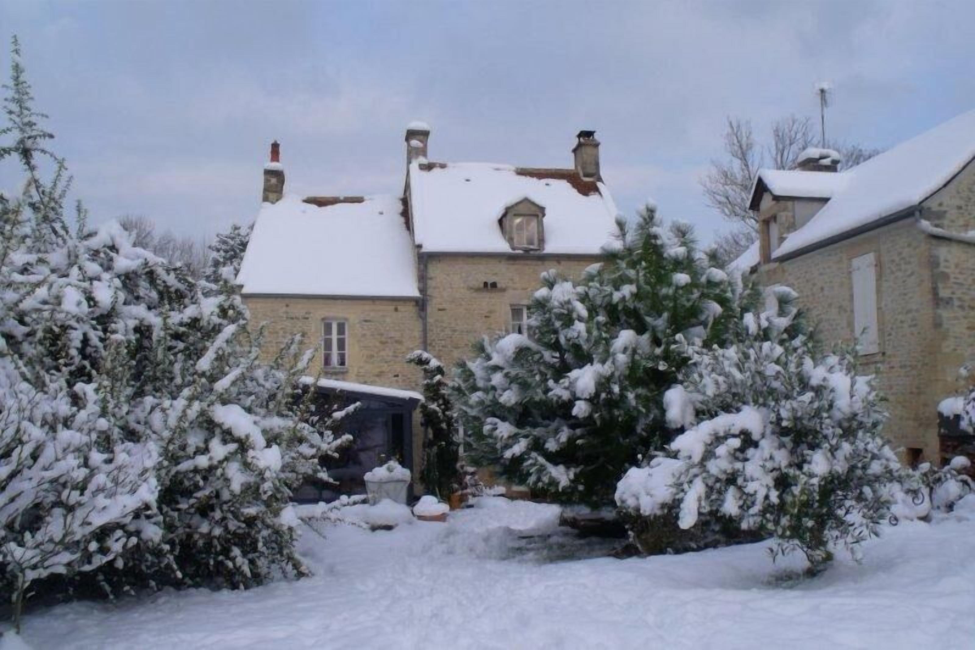 A stone building with a snow-covered roof and surrounding snow-covered trees.