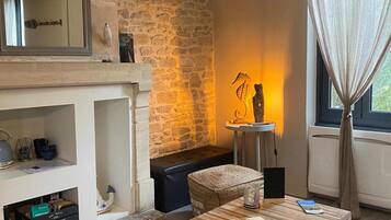 A cozy living room with a stone wall, a fireplace, a table with a plate of food, and a window with curtains.