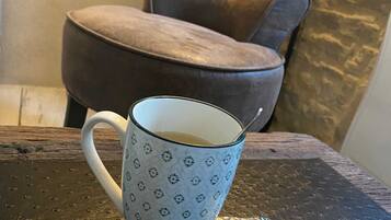 En vit mugg med ett blommönster står på ett bord med en strukturerad yta. Bredvid står en brun, klädd stol och en liten förpackning med kakor.