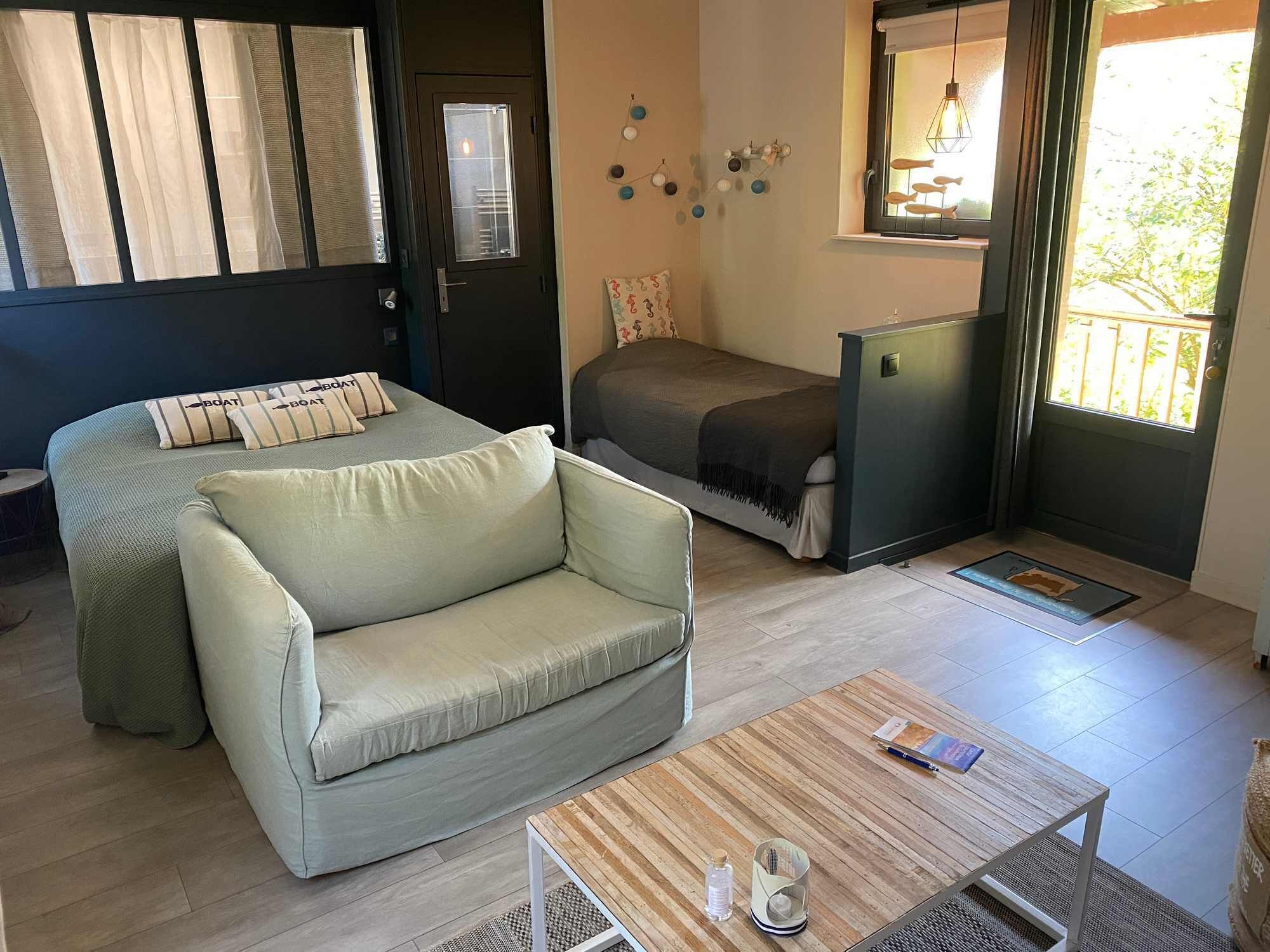 Un espacio habitable compacto con sofá, cama, una mesita y una ventana con cortinas.
