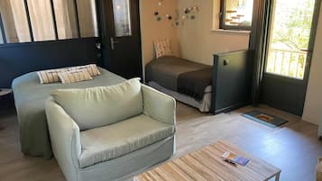 Un espacio habitable compacto con sofá, cama, una mesita y una ventana con cortinas.