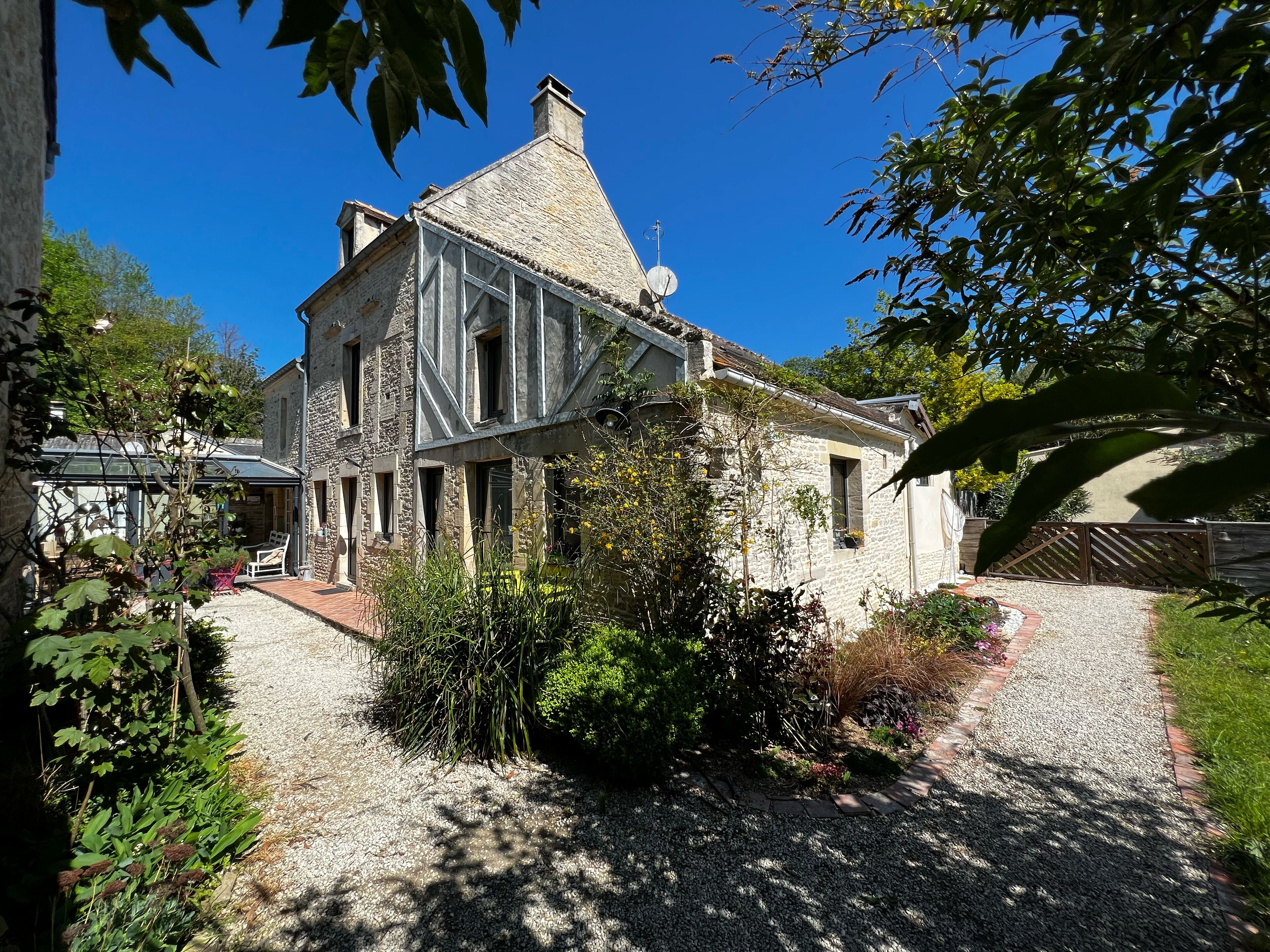 A stone house with a sloped roof, a covered porch, and a gravel driveway.