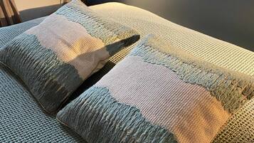 Un lit avec une couverture et des oreillers à motifs, une fenêtre avec des rideaux et un luminaire fixé au mur.