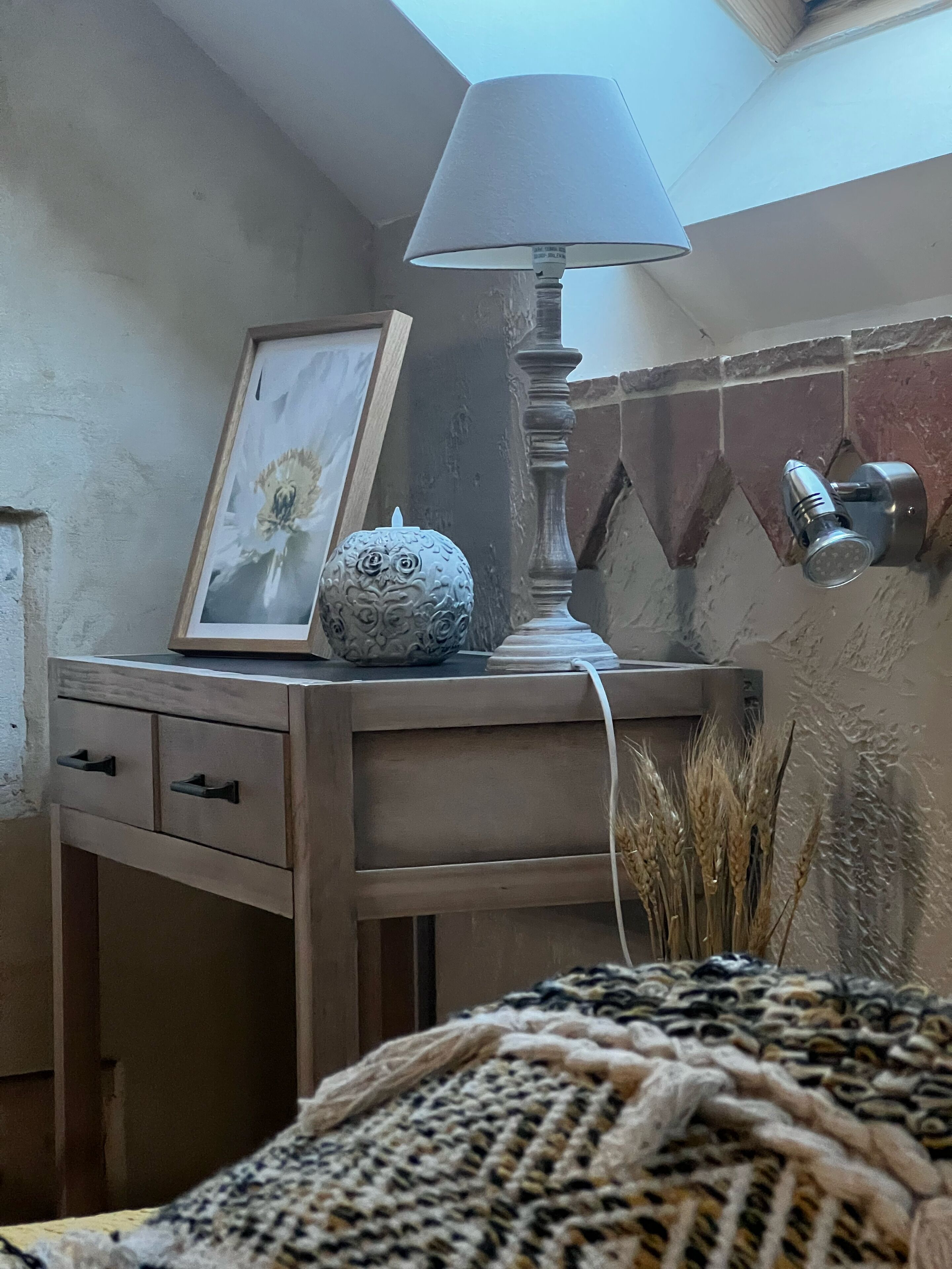Un dormitorio en esquina con una mesita de noche de madera, una lámpara, un cuadro enmarco y un adorno de búho decorativo.