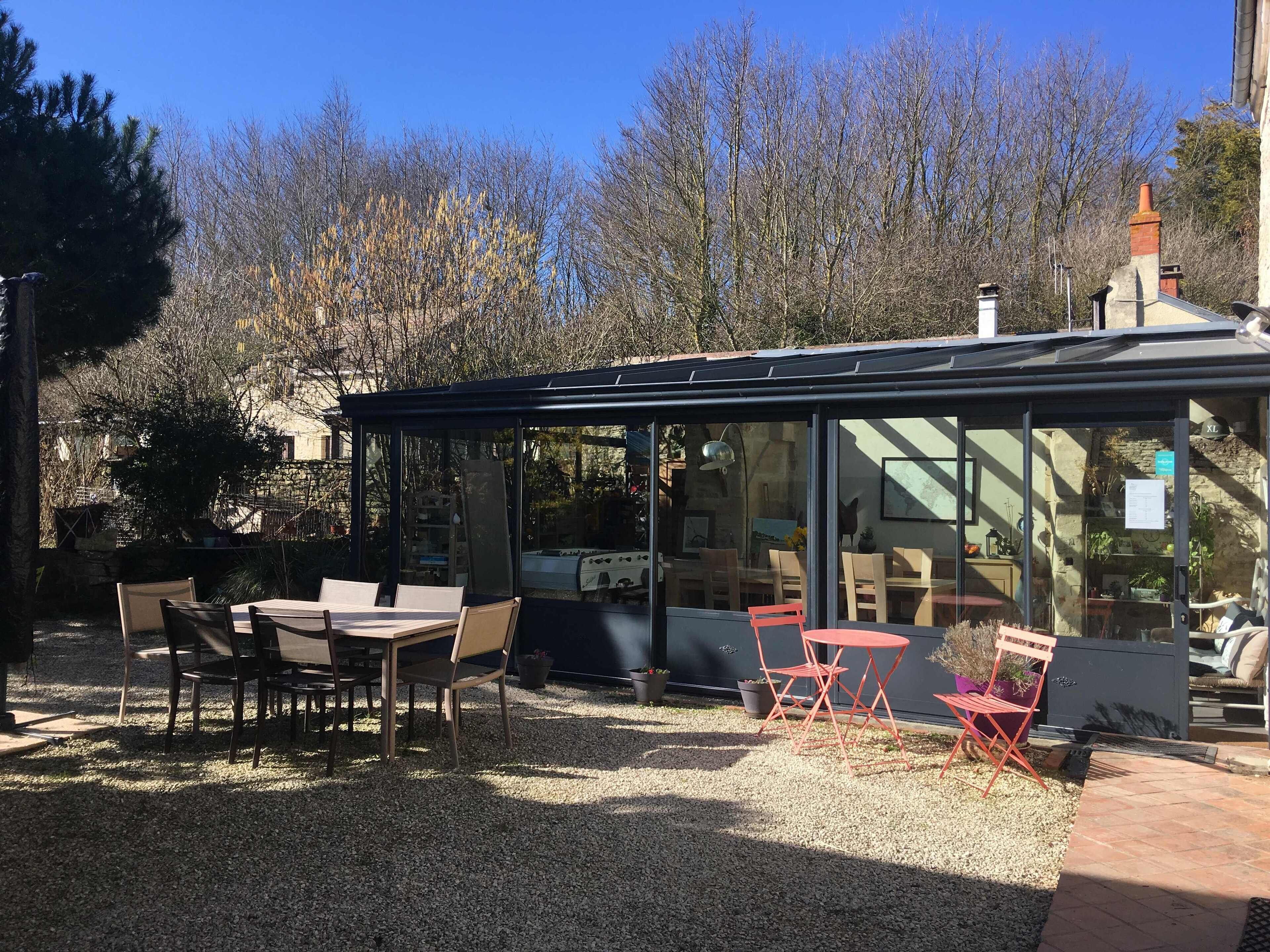 A covered outdoor seating area with tables and chairs, surrounded by gravel and trees.