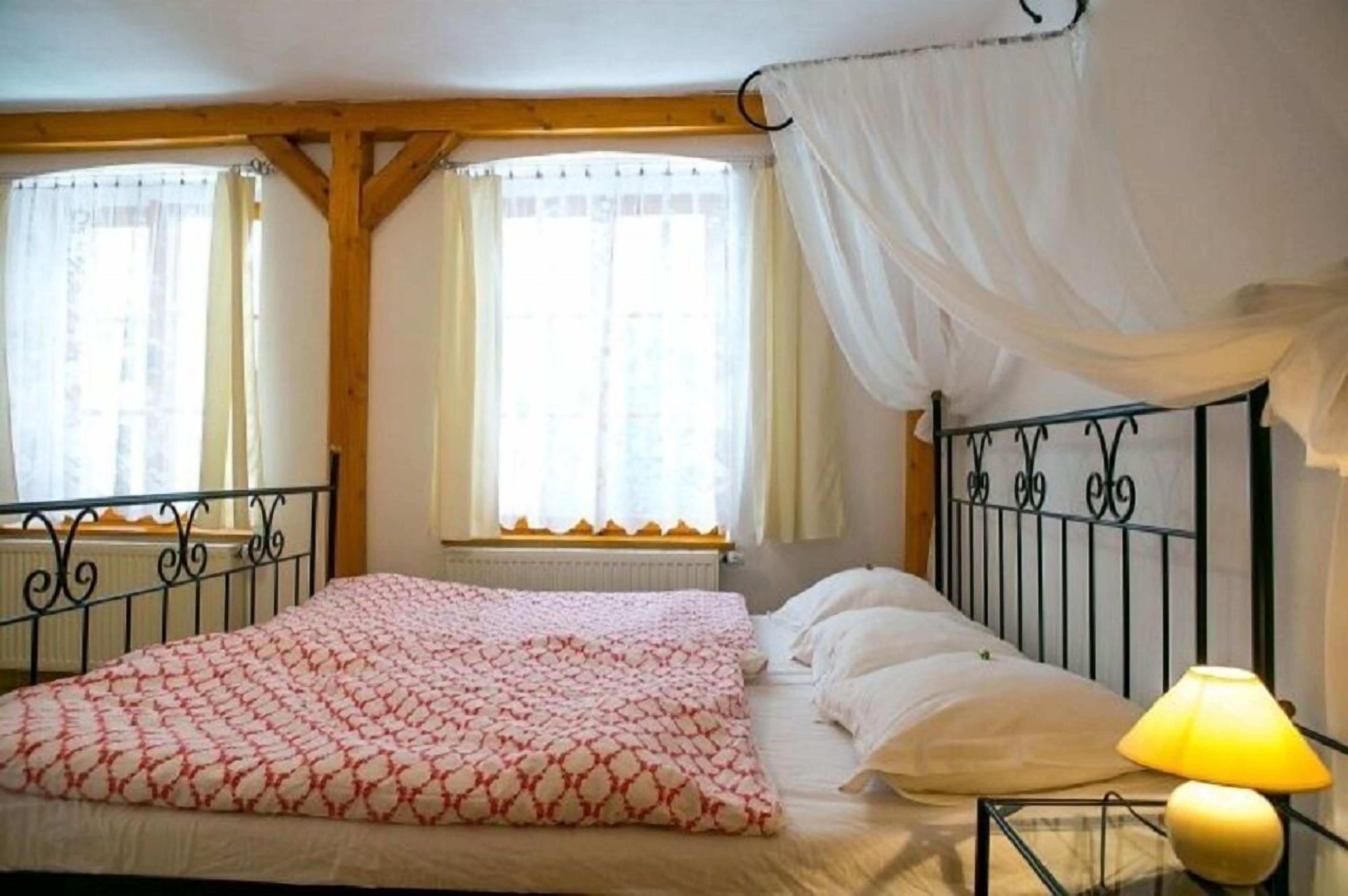 A bedroom with a bed, a window with curtains, a radiator, and a lamp on a bedside table.