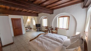 Un dormitorio con cama de madera, televisor, escritorio y ventanas arqueadas.