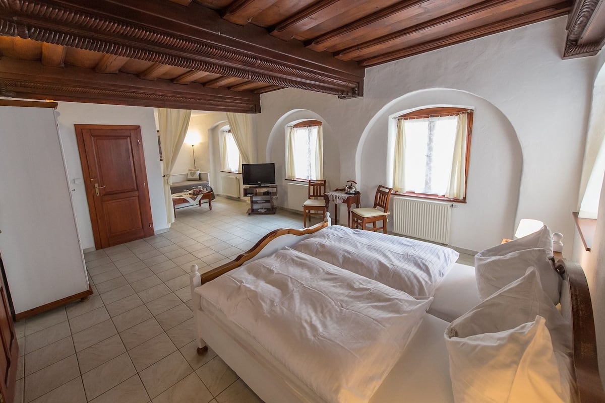 Un dormitorio con cama de madera, televisor, escritorio y ventanas arqueadas.