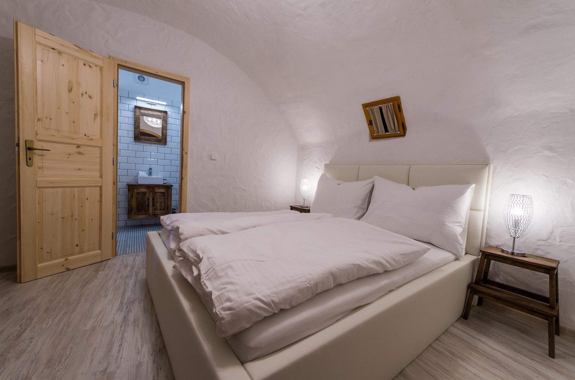 A bedroom with a large bed, a wooden door, a small bedside table, and a nightstand.
