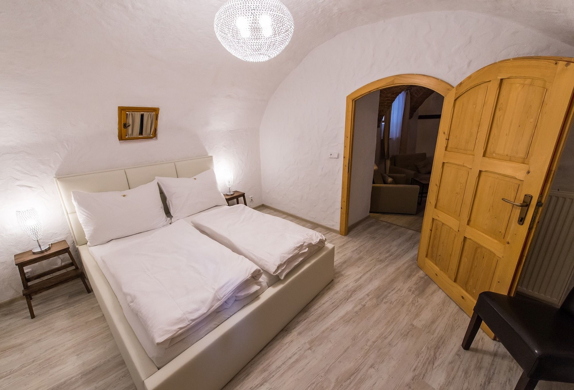 Un dormitorio con cama doble, mesitas de noche, una puerta de madera y un ventanal pequeño.
