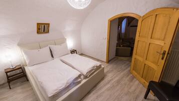 Un dormitorio con cama doble, mesitas de noche, una puerta de madera y un ventanal pequeño.