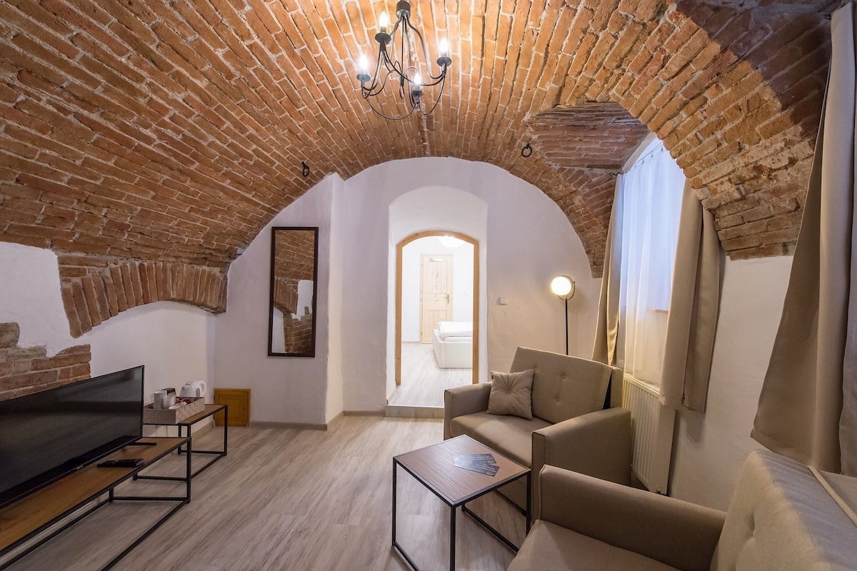 Una sala de estar acogedora con techo de ladrillo, un televisor de pantalla plana, un sofá y una mesa de centro.