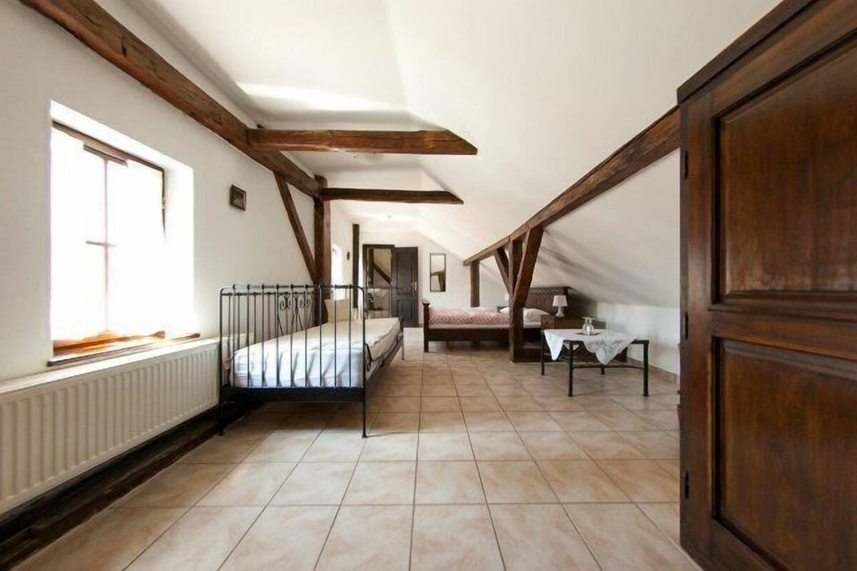 Una habitación con techo inclinado, vigas de madera a la vista, una cama, una mesita y un radiador.