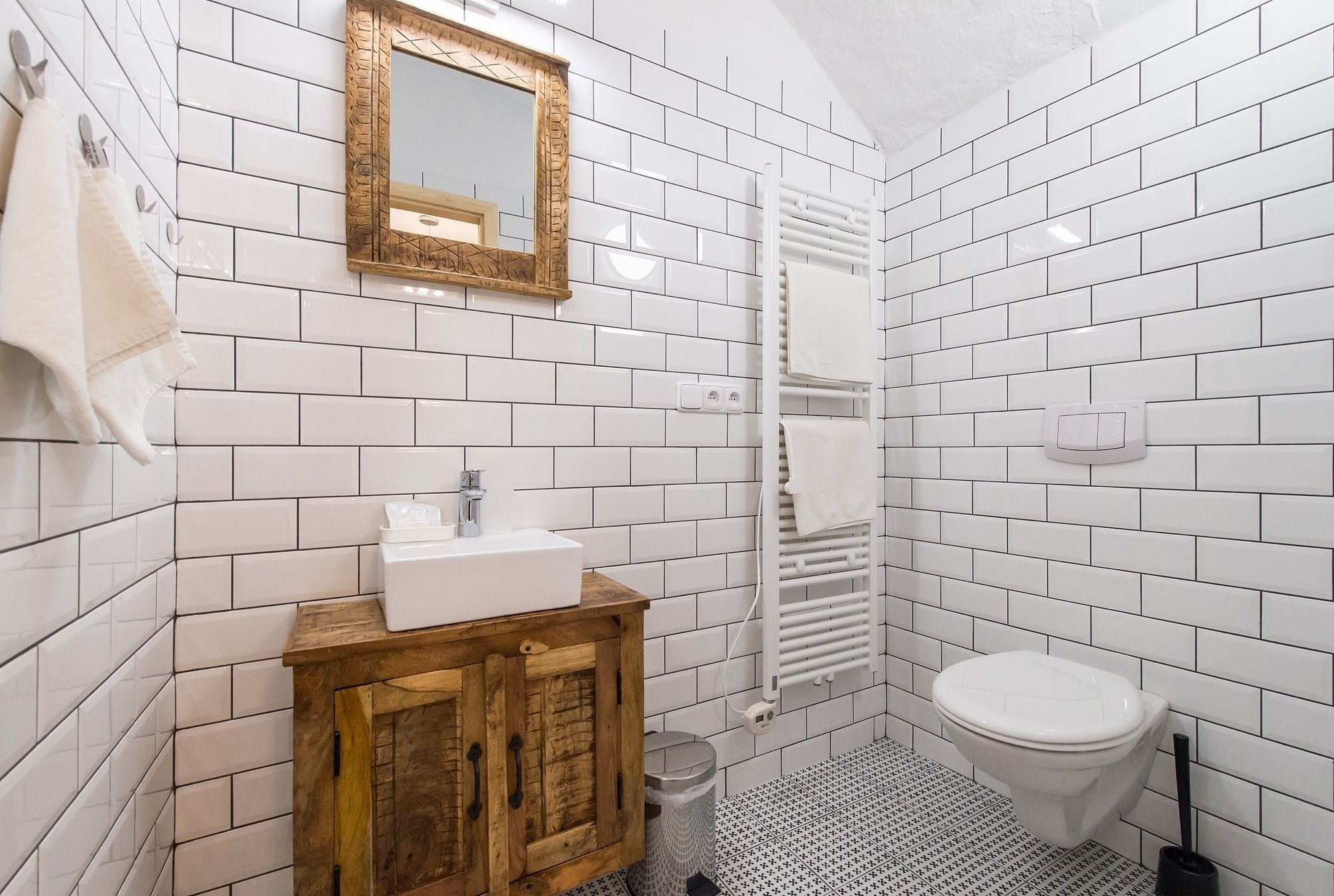 A bathroom with white subway tiles, a wooden cabinet, a sink, a toilet, a towel rack, and a mirror.