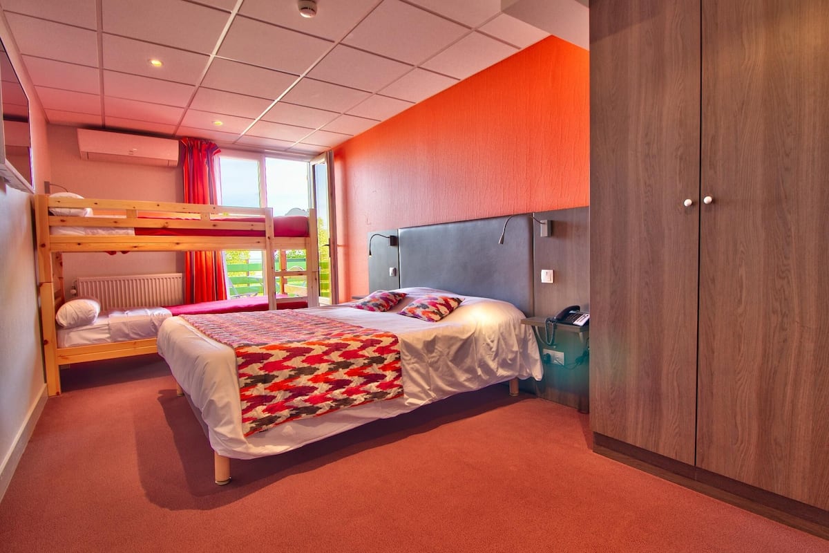 A hotel room with a bunk bed, a single bed, a wardrobe, and a view of the outdoors.