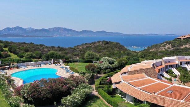 A resort with a swimming pool surrounded by sun loungers, a well-maintained garden, and a view of the sea and mountains. - Capo Ceraso Family Residence (Olbia)