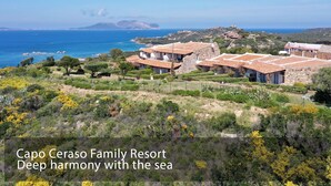 Ein Familienresort mit Steingebäuden und Terrakotta-Dächern, umgeben von viel Grün und mit Blick auf das Meer.