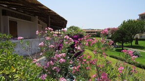 A courtyard with flowering plants, a building with a tiled roof, and a well-maintained lawn. - Capo Ceraso Family Residence (Olbia)