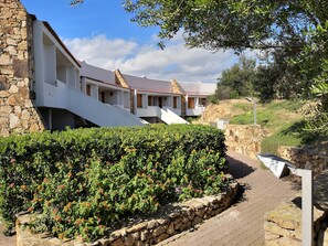 A building with white walls and red-tiled roofs, a stone pathway, and a well-maintained hedge with orange flowers. - Capo Ceraso Family Residence (Olbia)