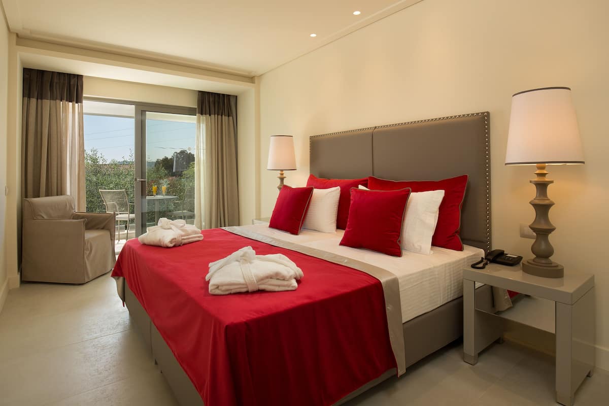A hotel room with a bed, two bedside lamps, a chair, a table, and a view of the outdoors.