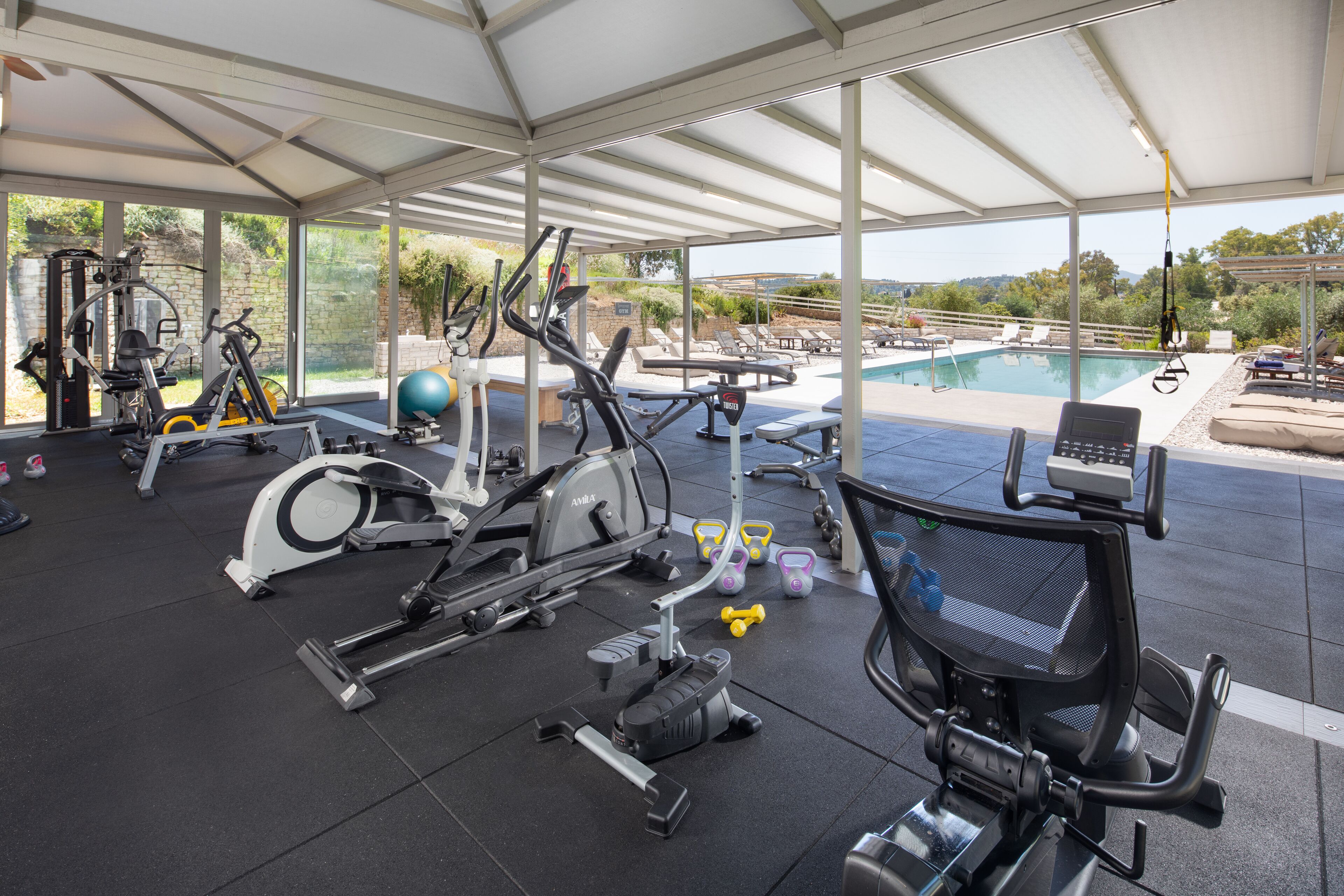 A covered gym area with exercise equipment, a pool, and outdoor seating.